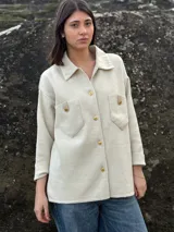 Camisa color crema tejida en lana, con cuello clásico, cierre frontal con botones dorados, dos bolsillos con solapa en el pecho y mangas largas con puños abotonados.