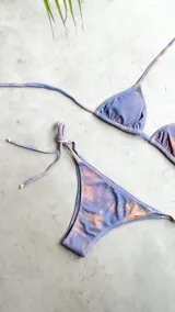 Bikini color dorado brillante, con corpiño triangular de atar al cuello y espalda, con almohadillas desmontables. La bombacha es vedetina con tiras ajustables a los costados.