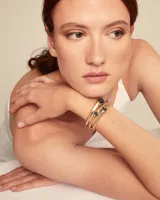 Pulsera rígida dorada de tres vueltas con apliques de cristales negros ovalados.