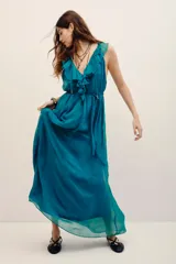 Vestido largo color verde turquesa, confeccionado en gasa con forrería a tono. Posee escote en V profundo con volados, sin mangas, y corte en la cintura con lazo ajustable.