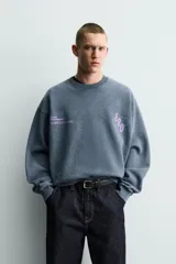 Sudadera de corte boxy fit con efecto lavado, cuello redondo y manga larga. Presenta estampados a contraste en color violeta en la parte frontal y acabados en rib en cuello, puños y ruedo.