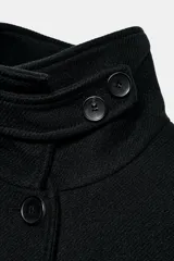 Abrigo corto de paño con mezcla de lana, color negro. Presenta cuello subido con cierre de botones, manga larga y dos bolsillos de plastrón con solapa en el frente. Cierre frontal con botones.