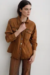 Chaqueta de denim color marrón, con corte entallado en la cintura, cierre frontal con botones metálicos y bolsillos superiores con solapa.