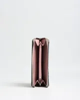 Billetera grande tipo fichero de cuero sintético color taupe, con cierre perimetral, detalles de tachas metálicas plateadas en los bordes y placa frontal con la inscripción de la marca Extra Large. Incluye una tira de mano desmontable con argolla metálica.