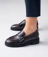 Mocasines de cuero color marrón con estampado de cocodrilo, detalle de hebilla metálica plateada y suela de goma negra. Diseño clásico con punta redonda y calce cómodo.