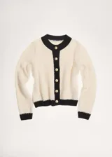 Chaqueta de punto de textura suave en color crema con detalles en contraste negro en cuello, puños, ruedo y tapeta de botones. Presenta un diseño recto, cuello redondo y cierre frontal con botones dorados.