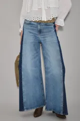 Jean de corte wide leg con diseño bicolor, presentando un panel central en denim lavado claro y paneles laterales en denim azul oscuro. Posee tiro alto y cierre frontal con botón.