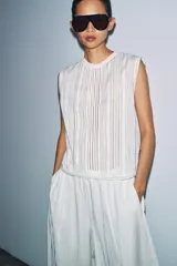Blusa sin mangas de algodón con cuello redondo, diseño con paneles verticales bordados y detalles de encaje, cierre posterior con abertura y botón.