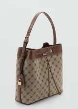 Bolso tipo bucket de diseño estructurado, confeccionado en tela con estampado geométrico en tonos marrón y beige, con detalles de cuero sintético marrón en la parte superior, base y asa. Cuenta con cierre de cordón ajustable y herrajes metálicos dorados.