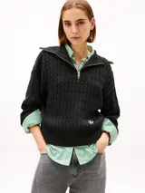 Sweater de punto negro con textura cableada, cuello alto con medio cierre de cremallera metálica dorada, mangas largas y detalle de logo bordado en el bajo.