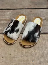 Sandalias bajas con base color suela y capellada de piel de vaca con manchas marrones y blancas.