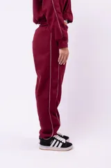 Conjunto deportivo compuesto por una campera con cierre y un pantalón de jogging, ambos de color negro con detalles de líneas blancas laterales. El pantalón presenta un corte holgado y cómodo.