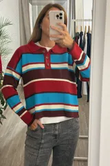 Sweater tejido de punto con diseño a rayas horizontales en colores rojo, azul, marrón y crema. Presenta cuello tipo polo con cierre frontal de tres botones y mangas largas.