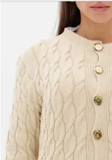 Cardigan de punto trenzado color beige, con cuello redondo, cierre frontal con botones dorados y mangas largas con puños acanalados.
