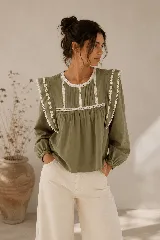 Blusa verde militar de 100% algodón, con cuello redondo, mangas largas con puños elastizados y detalles de puntillas y bordados en el frente y en los hombros.