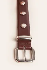 Cinto de cuero color suela con tachas metálicas circulares y hebilla plateada.