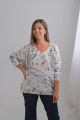 Sweter de punto con corte amplio, escote en V y mangas largas. Presenta un diseño estampado abstracto sobre una base color crudo con detalles en tono dorado.