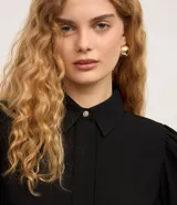 Camisa de crepé color blanco, con cuello inglés, manga larga abullonada con puños abotonados y cierre frontal oculto con botón diferenciado en el cuello.