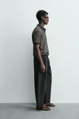 Polo de manga corta con cuello solapa y cierre frontal de dos botones. Tejido de punto con textura de rombos en tonos negro y beige, con ribetes negros en cuello, mangas y bajo.