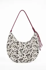 Cartera tipo hobo con estampado animal print en tonos blancos y negros, asa de cuerda bordó y detalles de nudos y cuentas colgantes.