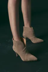 Botas de gamuza color arena, con taco fino y punta fina. Presenta una abertura en forma de V en el frente y detalle de costuras horizontales en el empeine.