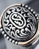 Anillo de plata y oro de diseño ovalado, con detalles grabados y filigrana en relieve en la parte superior.