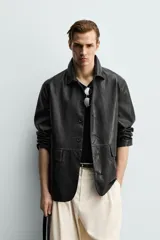Sobrecamisa de corte relaxed fit confeccionada en tejido efecto piel de color negro, con cuello solapa, manga larga, bolsillos con solapa en la cadera y cierre frontal de botonadura.