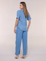 Blusa de silueta amplia de lyocell color azul con diseño de rayas verticales blancas. Cuenta con cuello mao abierto, abotonadura frontal, mangas cortas caídas y lazos en el ruedo para anudar al frente.