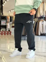 Pantalón de jogging oversize negro con felpa, de corte recto y cordón ajustable en la cintura. Presenta un pequeño estampado de texto blanco en el lateral izquierdo.