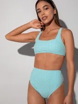Conjunto de bikini con corpiño estilo top deportivo y bombacha de tiro alto, ambos con estampado a cuadros vichy en tonos celeste y blanco.