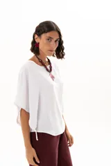 Blusa blanca de corte holgado y diseño minimalista, con mangas cortas tipo murciélago que presentan un detalle de fruncido lateral con cordón ajustable.