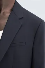 Blazer de corte regular fit confeccionado en tejido con lana. Presenta cuello con solapas de muesca, cierre frontal de un botón, bolsillos de vivo en el pecho y en la cadera, y aberturas en la espalda.