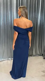 Vestido largo de fiesta color azul marino con acabado brillante y efecto glitter. Presenta un diseño con escote tipo hombros caídos y detalle de drapeado en la cintura que estiliza la figura.