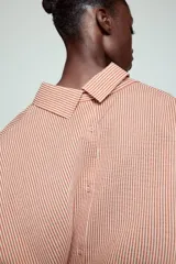 Camisa de cuello solapa y manga larga con estampado de rayas verticales. Presenta un bolsillo de plastrón en el delantero, cierre frontal con botones y detalle de botones en la espalda. Su diseño cuenta con un bajo asimétrico y aberturas laterales.