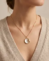 Collar de bronce con cadena fina tipo veneciana y un dije circular con fondo de nácar y relieve de sol dorado.