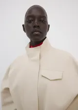 Chaqueta beige de cuello alto, manga larga con puños abotonados, bolsillo con solapa en el pecho, cinturón ajustable para la cintura y cierre frontal de cremallera oculta.