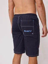Short de baño negro con cordón ajustable en la cintura, bolsillos laterales y logo de la marca Rusty estampado en la pierna izquierda.