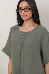 Vestido midi de lino color beige, con mangas cortas, cuello redondo, alforzas verticales en el pecho y detalle de volados en el ruedo.