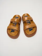 Sandalias de cuero vacuno color marrón con acabado brillante, diseño de dos tiras anchas acolchadas y plataforma baja.