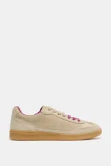 Zapatilla deportiva de gamuza en color beige, con cordones y forro interior en color fucsia, montada sobre una suela de goma color caramelo.