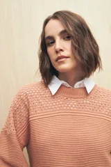Sweater de punto color salmón con cuello redondo y mangas anchas. Presenta un diseño calado en la parte superior y tejido tramado horizontal en el resto del cuerpo.
