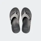 Ojotas Reef Cushion Phantom, base negra y tiras grises con logo de la marca.