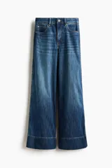 Jean de cinco bolsillos en denim con leve stretch, tiro alto y pierna amplia de corte holgado. Presenta ribete trenzado en los laterales y doblez cosido en el bajo, con diseño inspirado en los años 70.