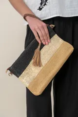 Sobre de mano de rafia con diseño de franjas horizontales en negro, dorado y beige. Incluye lazo de mano y correa para colgar.