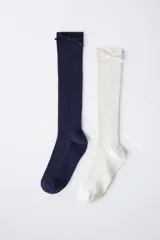 Pack de dos pares de calcetines altos de tejido acanalado, uno en color azul marino y otro en color blanco, ambos con un pequeño aplique de lazo decorativo en la parte superior.