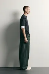 Pantalón barrel fit de mezclilla color verde militar, con efecto lavado, cinco bolsillos, cierre frontal con cremallera y botón, y detalle de pinzas en las rodillas.