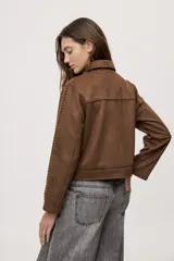 Campera negra de efecto gamuzado con cuello camisero, cierre frontal de botones, bolsillos plaqué en el pecho y detalles de costuras decorativas y calados.
