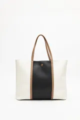 Cartera amplia tipo tote bag en símil cuero, con diseño en bloques de color blanco, negro y beige. Tiene asas largas de color marrón claro y un detalle metálico dorado en el centro.