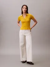 Chomba de punto pointelle texturizado color amarillo, con cuello tipo Johnny abierto, manga corta y ribetes en canalé. Presenta un diseño minimalista con logo bordado sutil en la parte frontal.