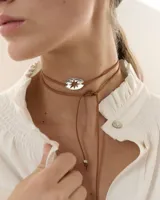 Choker tipo bolo tie con cordón de gamuza marrón y dije central ovalado de acrílico espejado con diseño de estrella calada. El diseño permite múltiples formas de uso gracias a su largo ajustable.